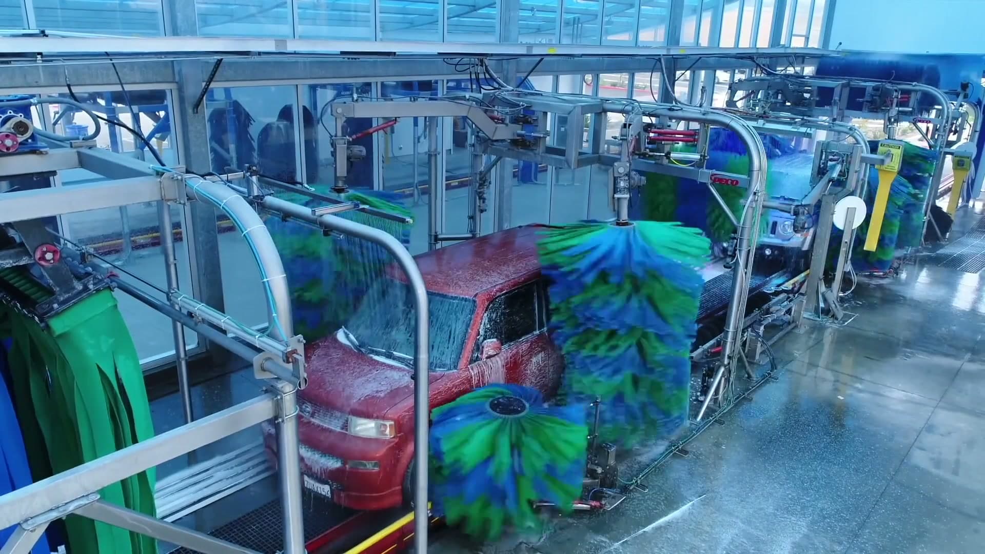 A vehicle moving through Buff-N-Shine's wet wash tunnel with blue and green brushes